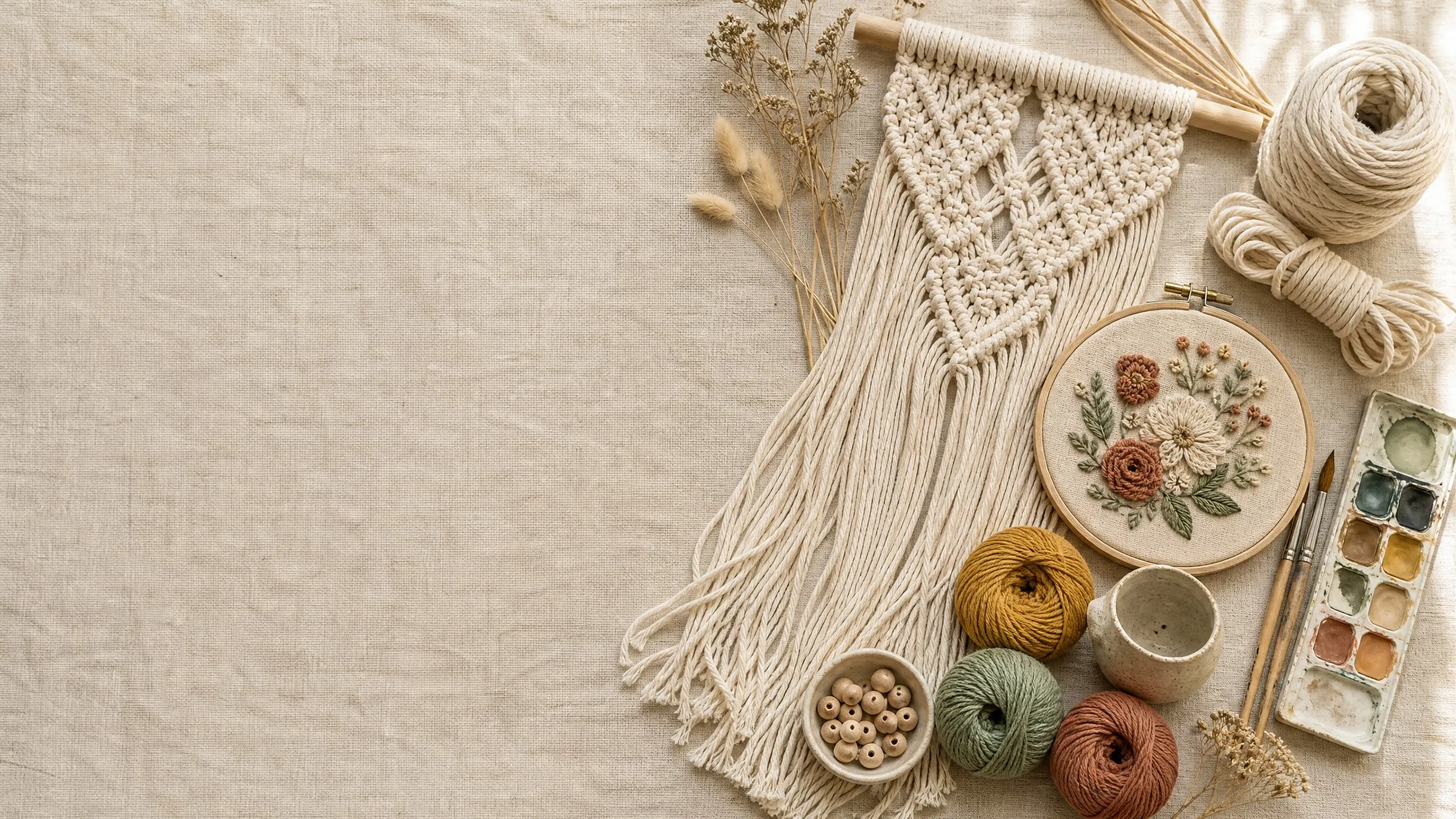 An art studio worktable seen from above, with macramé, an embroidery hoop, wool and a watercolour palette